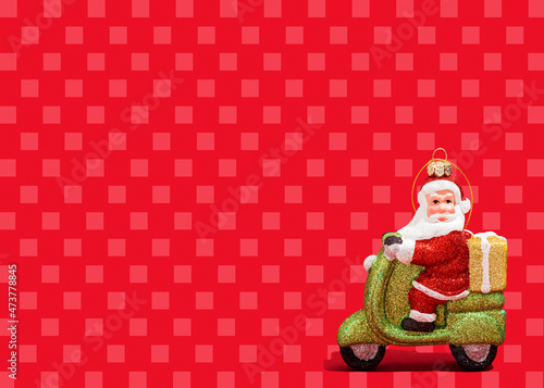 Christmas ornament of Santa Claus riding motor scooter against vibrant red checked background photo