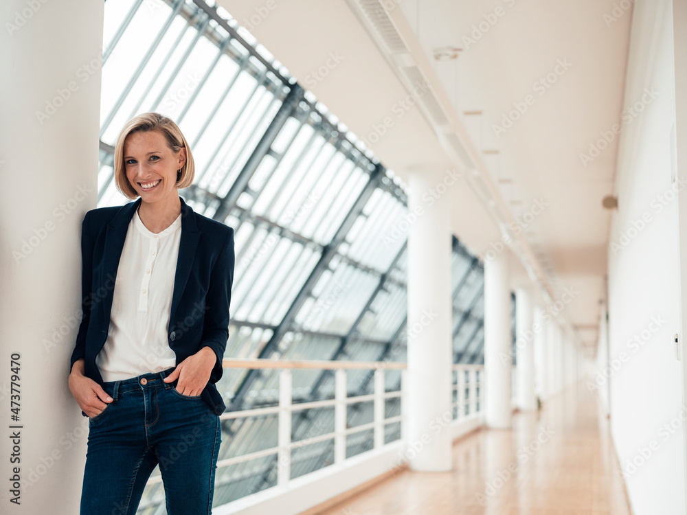 Female entrepreneur with hands in pockets standing at office corridor Female entrepreneur with hands in pockets standing at office corridor
