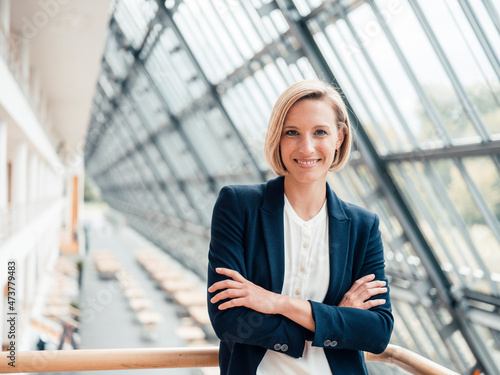 Smiling businesswoman with arms crossed leaning on railing in office photo