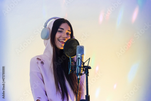 Smiling female singer wearing hooded top singing at studio photo