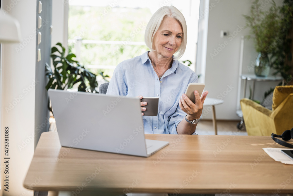 Mature female professional using smart phone at desk in home office Mature female professional using smart phone at desk in home office