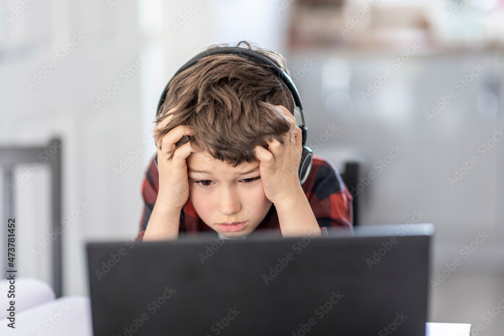 Tired boy attending remote classes through laptop at home Tired boy attending remote classes through laptop at home