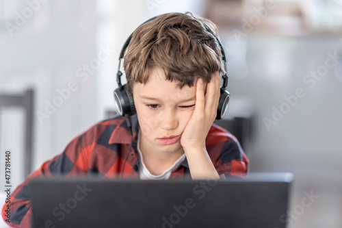 Boy getting bored during online classes attending at home photo