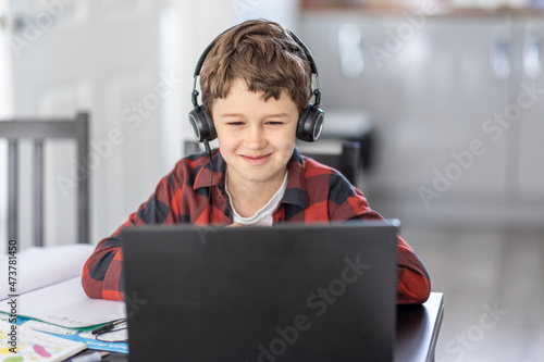 Smiling boy attending online classes through laptop while e-learning at home photo