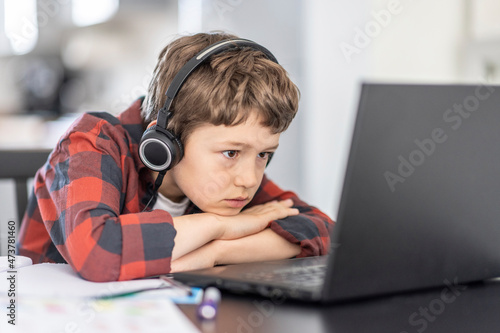 Boy attending online classes through laptop while e-learning at home photo