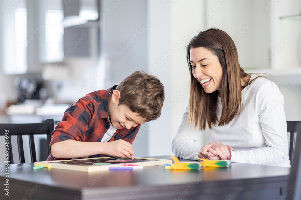 Smiling mother looking at son drawing on slate in kitchen Smiling mother looking at son drawing on slate in kitchen