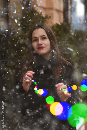 Lovely lady walking at the street with garlands during snowfall
