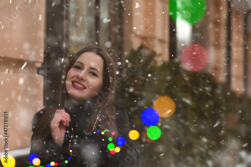 Attractive lady walking at the street with garlands during snowfall