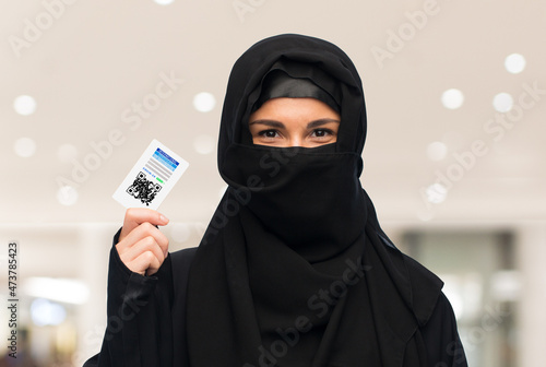 pandemic, health and people concept - woman in hijab with immunity passport qr code over shopping mall background
