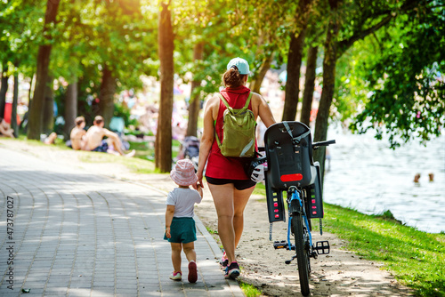 A woman with her daughter and a bicycle walks in the park 