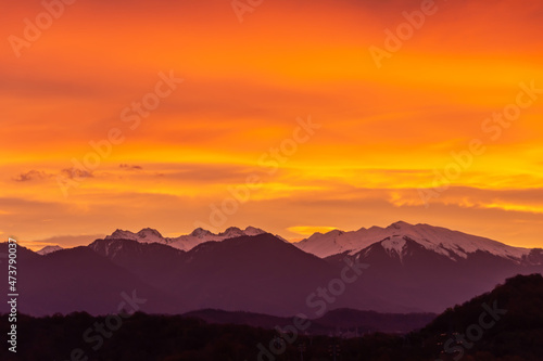Bright orange beautiful clouds dawn over a snow-capped mountain range.