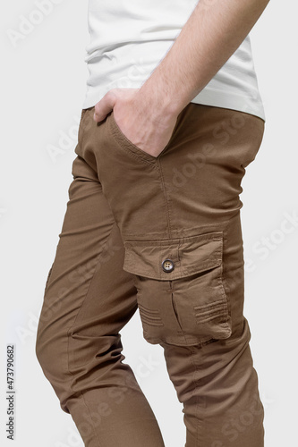Side view of man wearing brown cargo pants with hand in pocket on grey background.