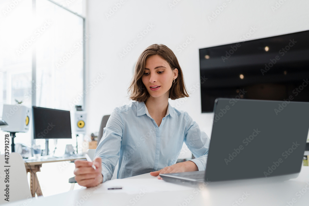 Young female professional sitting with laptop while working in office Young female professional sitting with laptop while working in office