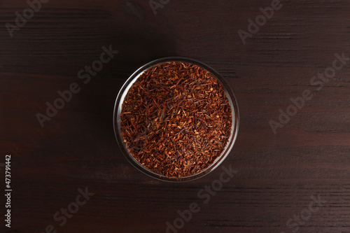 Dry rooibos leaves in glass bowl on wooden table  top view