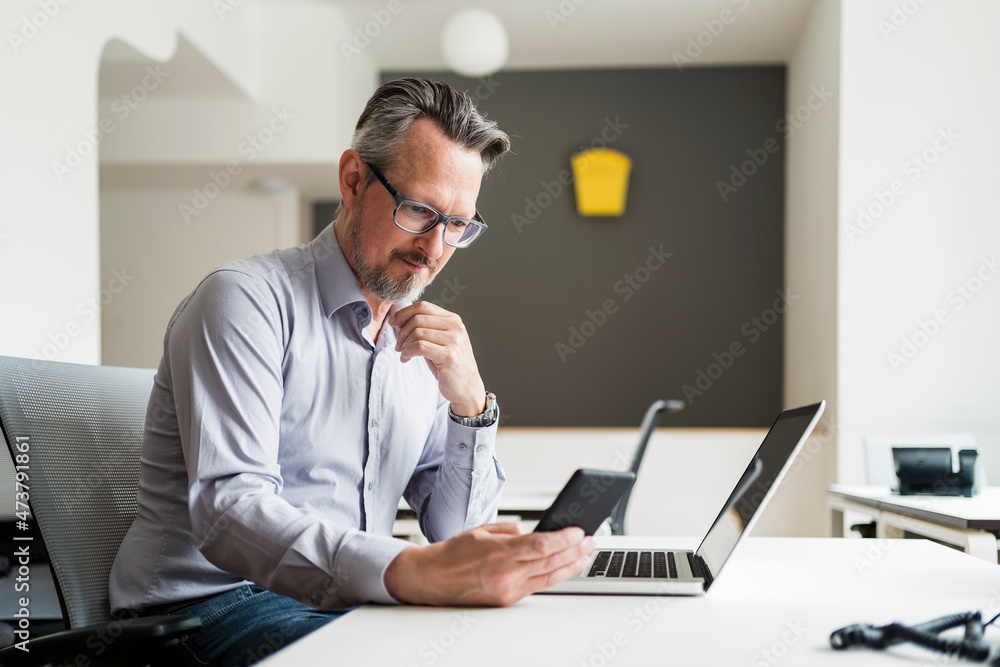 Male entrepreneur using mobile phone while sitting by desk Male entrepreneur using mobile phone while sitting by desk