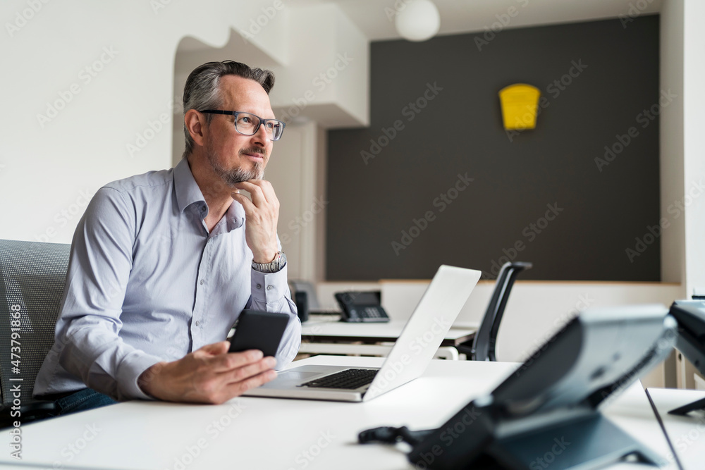 Thoughtful with hand on chin looking away while sitting at desk