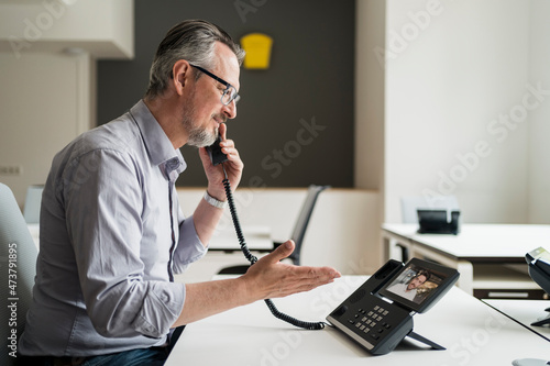 Male entrepreneur talking with colleague through VoIP telephone in office photo