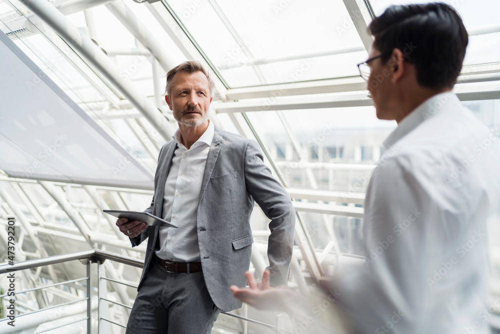 Businessman holding digital tablet while discussing with colleague in office Businessman holding digital tablet while discussing with colleague in office