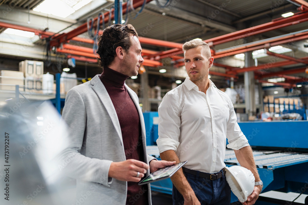 Businessman discussing with male engineer while walking at industry Businessman discussing with male engineer while walking at industry