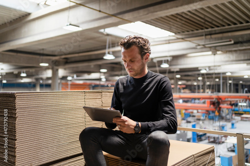 Businessman using digital tablet while sitting on cardboard stack photo