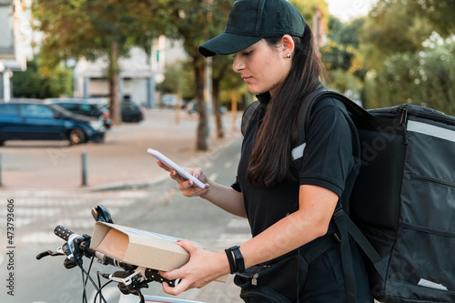 Young female delivery person scanning package with smart phone