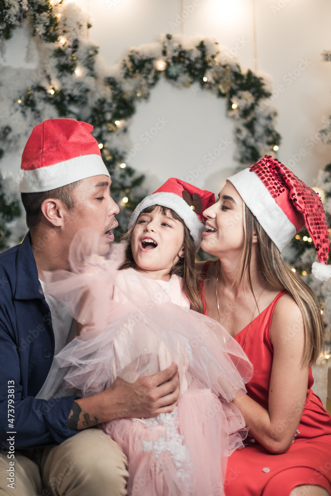 Christmas studio family shoot in red Christmas hats. New Year photo of happy mixed family with cute daughter. Everyone smile and laugh