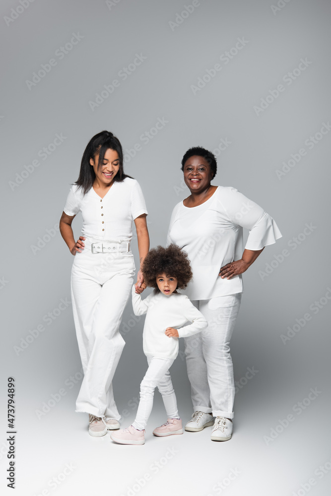 smiling african american women and girl in white clothes posing with hands on hips on grey smiling african american women and girl in white clothes posing with hands on hips on grey