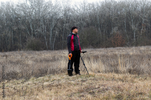 a man with a metal detector and a shovel walks in a clearing near the forest