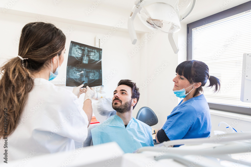 Female dentist with assistant explaining x-ray to patient at medical clinic Female dentist with assistant explaining x-ray to patient at medical clinic