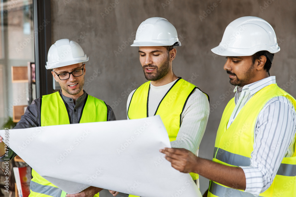 architecture, construction business and people concept - male architects in helmets with blueprint working in office building architecture, construction business and people concept - male architects in helmets with blueprint working in office building
