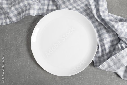 Empty white plate on gray stone table with checkered blue linen napkin. Flat lay, top view, copy space