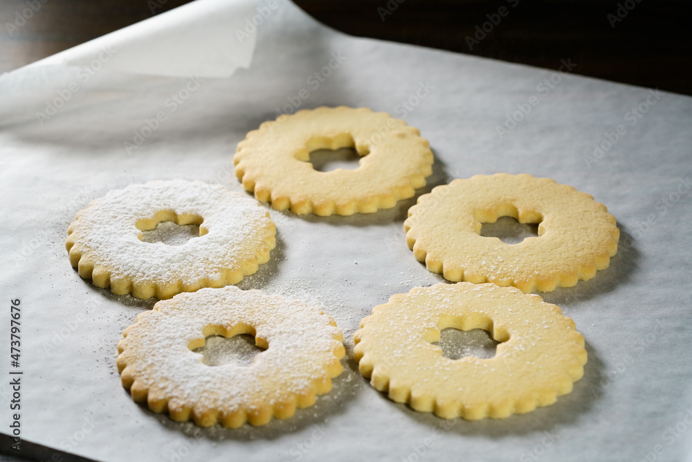 Making Linzer cookies, sprinkling tops with powdered sugar. White parchment paper, dark background, high resolution