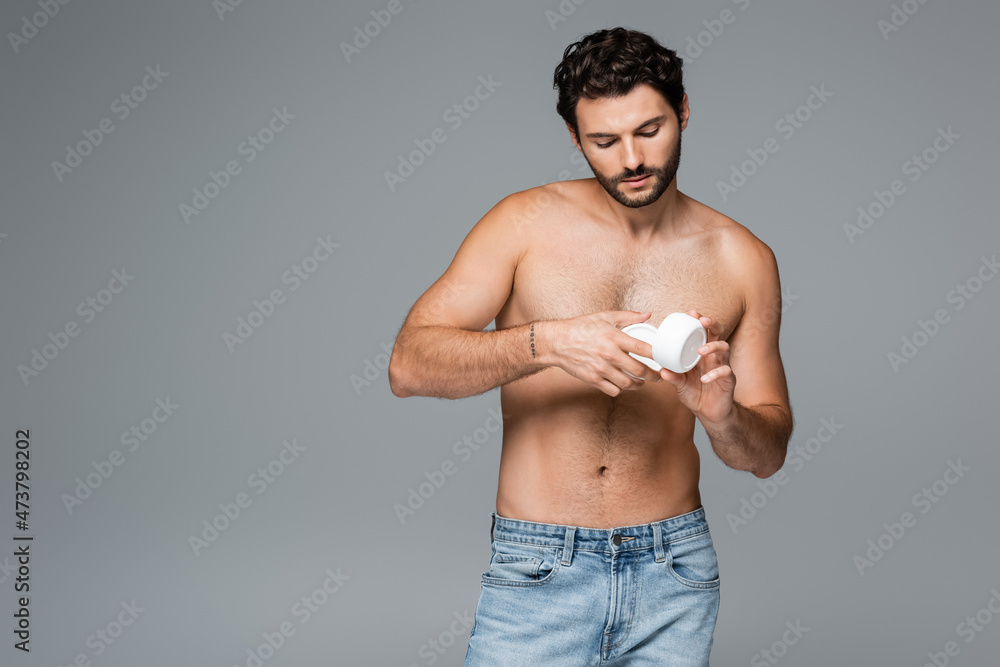 tattooed and shirtless man holding container with cosmetic cream isolated on grey