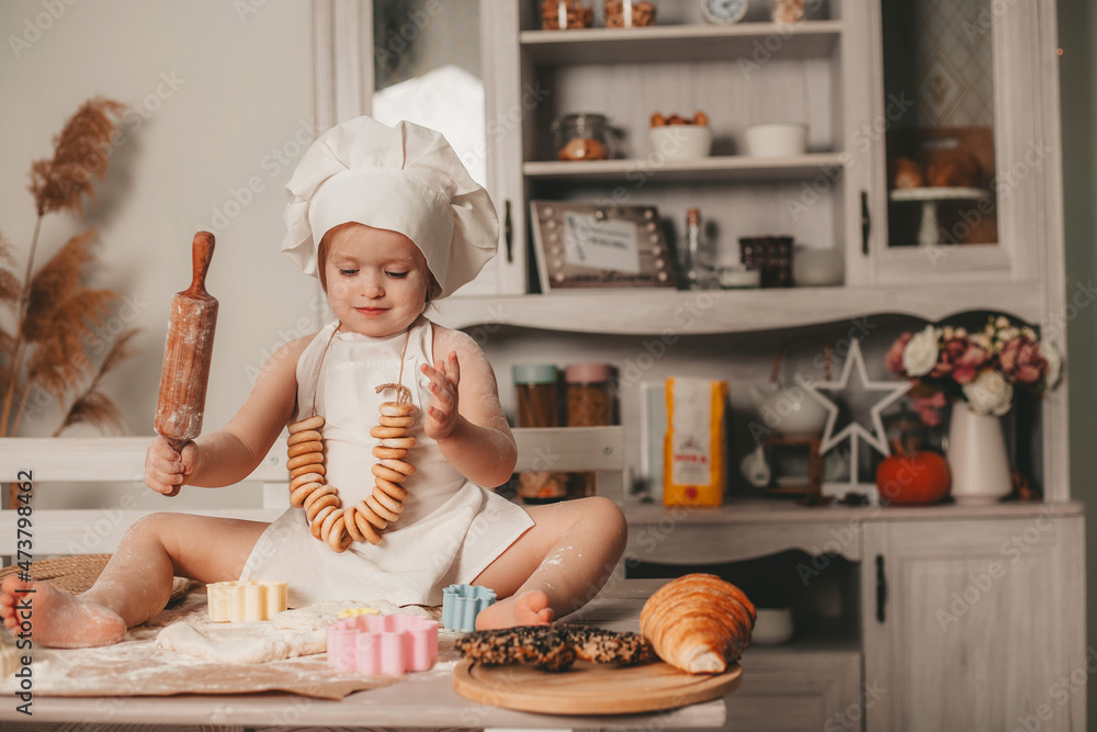 charismatic girl in an apron and a hat is sitting and rolling out the dough charismatic girl in an apron and a hat is sitting and rolling out the dough