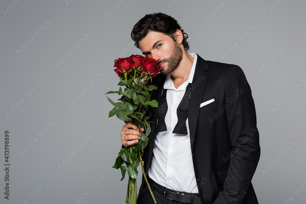 bearded man in suit smelling red roses while looking at camera isolated on grey bearded man in suit smelling red roses while looking at camera isolated on grey