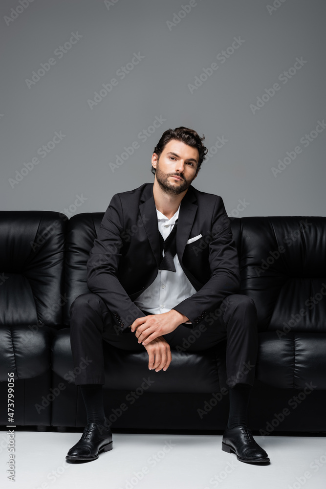 bearded man in suit sitting on black leather sofa on grey bearded man in suit sitting on black leather sofa on grey