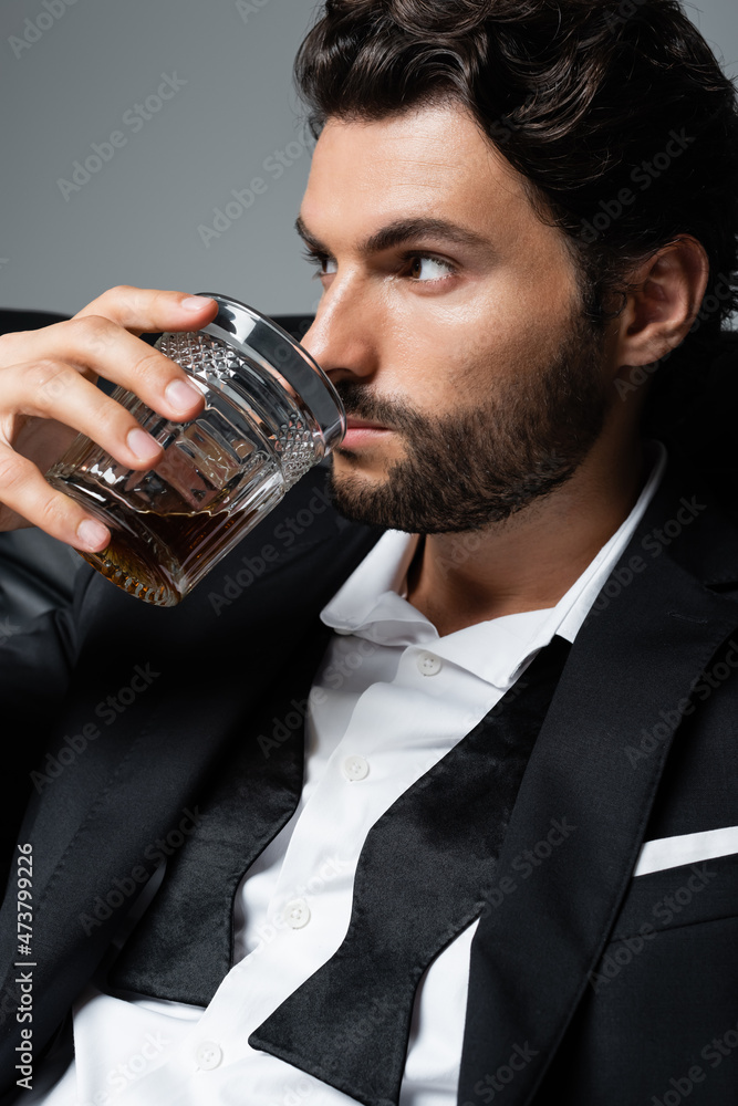 bearded man with wavy hair drinking brandy isolated on grey bearded man with wavy hair drinking brandy isolated on grey