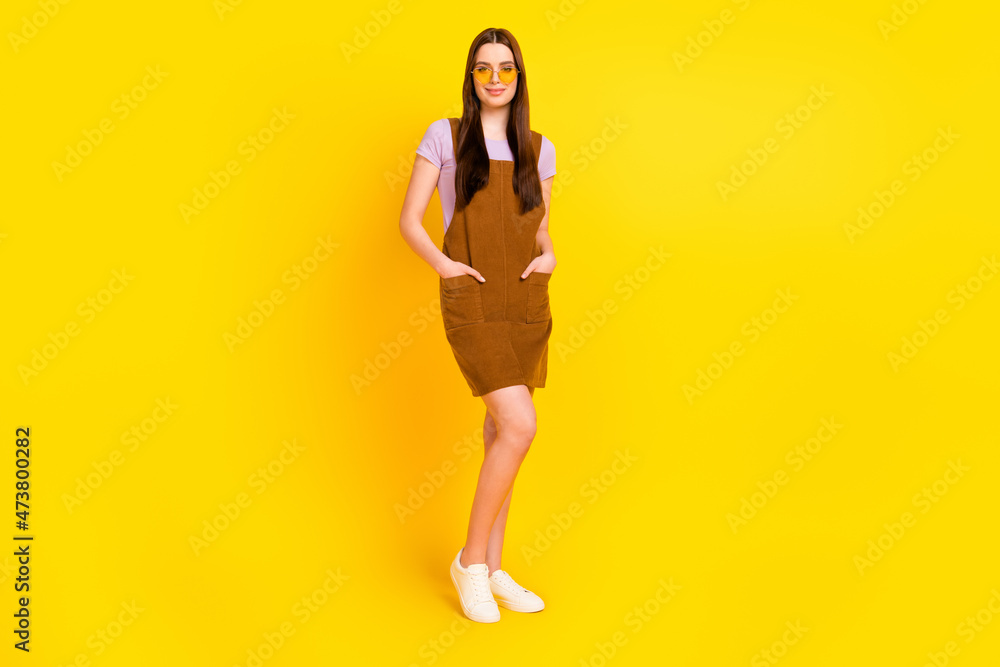 Full length body size view of attractive cheerful girl posing holding hands in pockets isolated over bright yellow color background Full length body size view of attractive cheerful girl posing holding hands in pockets isolated over bright yellow color background