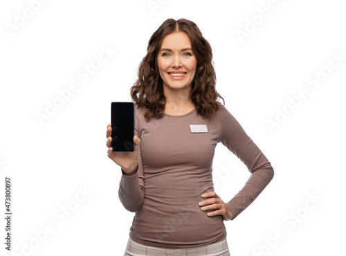 sale, shopping and business concept - happy female shop assistant with name tag showing smartphone over white background