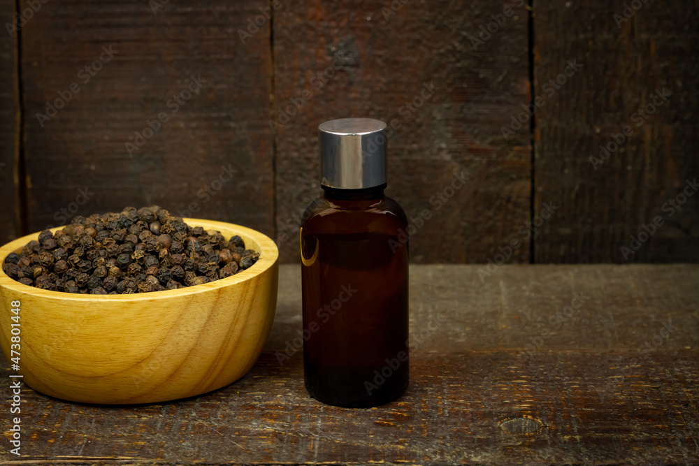 Black pepper essential oil in glass bottle with peppercorn on wooden bowl on rustic wooden background. Black pepper essential oil in glass bottle with peppercorn on wooden bowl on rustic wooden background.