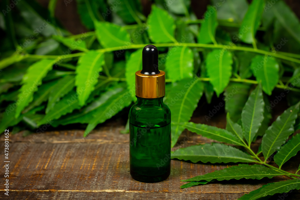 Neem oil in bottle and neem leaf with branch on wooden background.