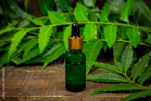 Neem oil in bottle and neem leaf with branch on wooden background.
