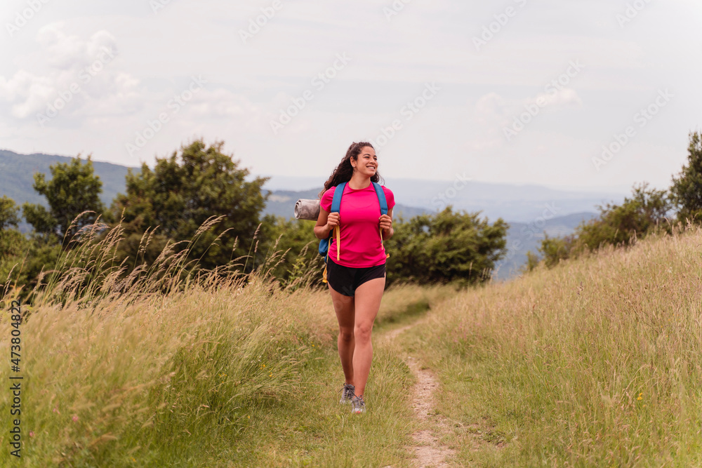 Smiling female hiker looking away while walking through meadow Smiling female hiker looking away while walking through meadow