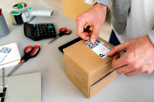 Male entrepreneur sticking QR code on cardboard package at desk photo