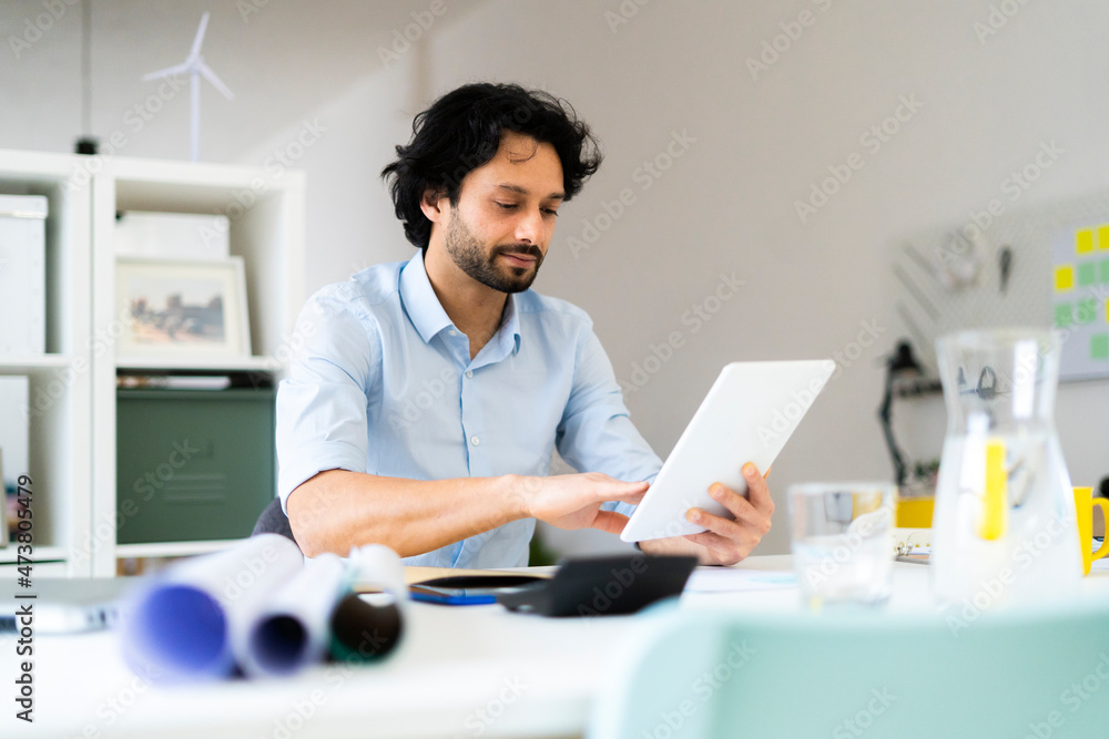 Young male entrepreneur using digital tablet while sitting at office Young male entrepreneur using digital tablet while sitting at office
