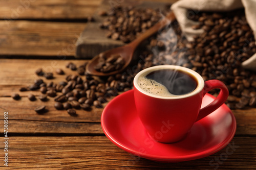 Cup of aromatic hot coffee and beans on wooden table. Space for text