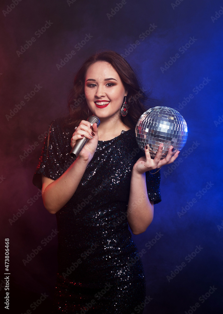 Naklejka premium Party happy woman wearing black dress with disco ball and microphone