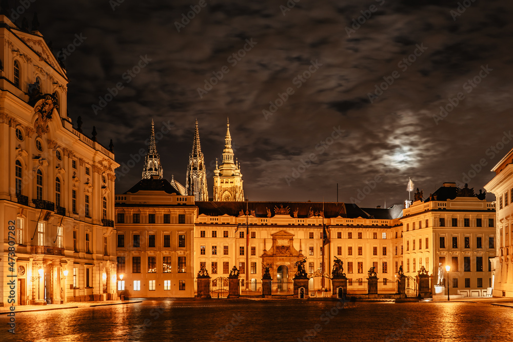 Main gate of Prague Castle with statues at night, illuminated St Vitus Cathedral in background.UNESCO site,Famous travel destination.Evening city lights,no people,romantic atmosphere with moonlight