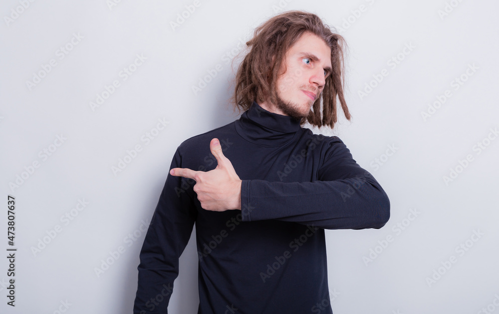 Young man pointing or show direction. The man looks to the side and points his arm to the left over gray background copy space Young man pointing or show direction. The man looks to the side and points his arm to the left over gray background copy space