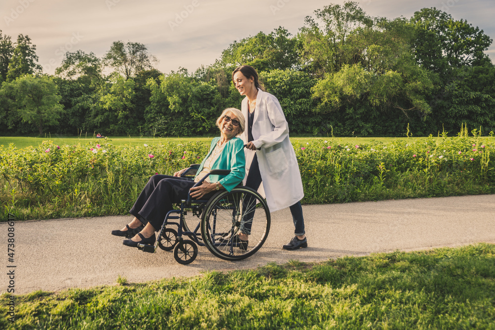 Smiling senior woman in wheelchair with caretaker in park Smiling senior woman in wheelchair with caretaker in park